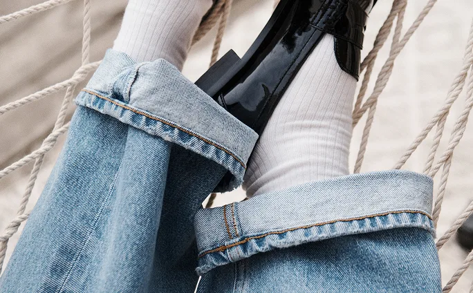 Close-up of a person lounging in a hammock, wearing rolled-up denim jeans and cotton socks.